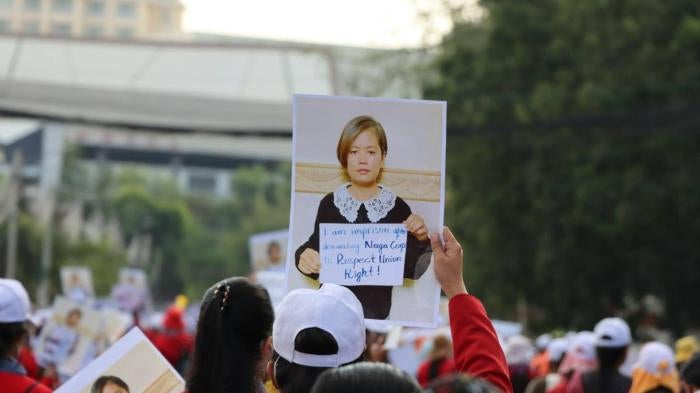 A crowd at a protest holds up a sign of a photo of a women 