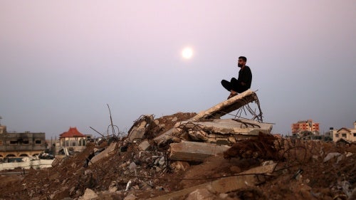 The moon rises as a man sits atop a pile of rubble it al-Bureij refugee camp in central Gaza Strip on November 15, 2024, amid ongoing hostilities in Gaza.
